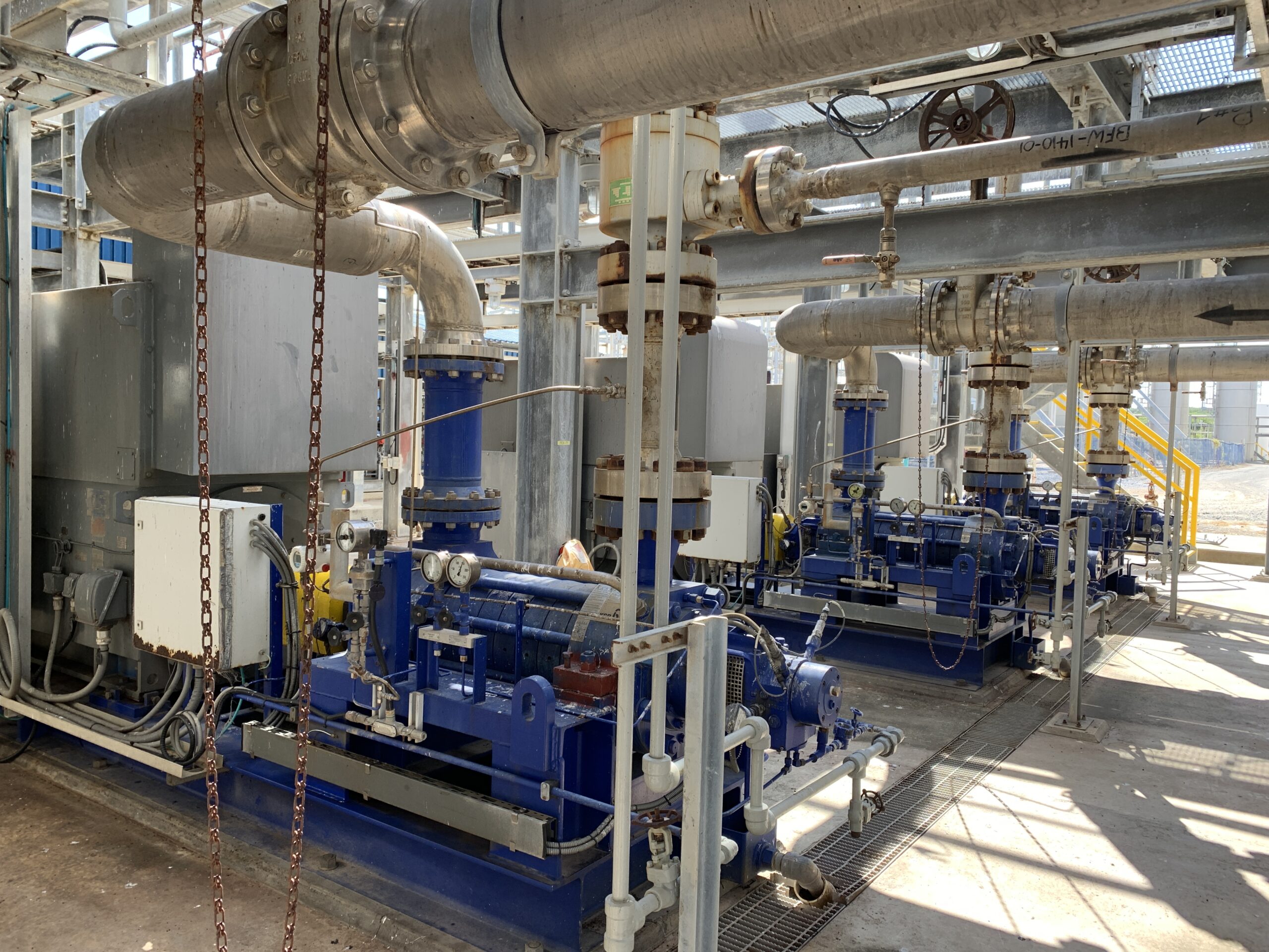 Interior view of an oil and gas facility, filled with complex machinery, pipes, control panels, and operators in safety gear overseeing operations.