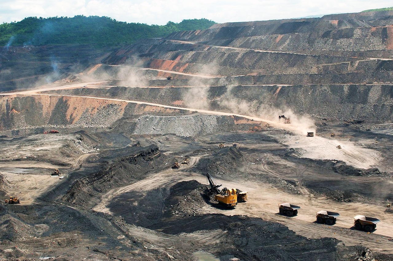 Aerial view of mine and mining equipment, consisting of an excavator and three haul trucks following behind it and a haul truck off in the distance.