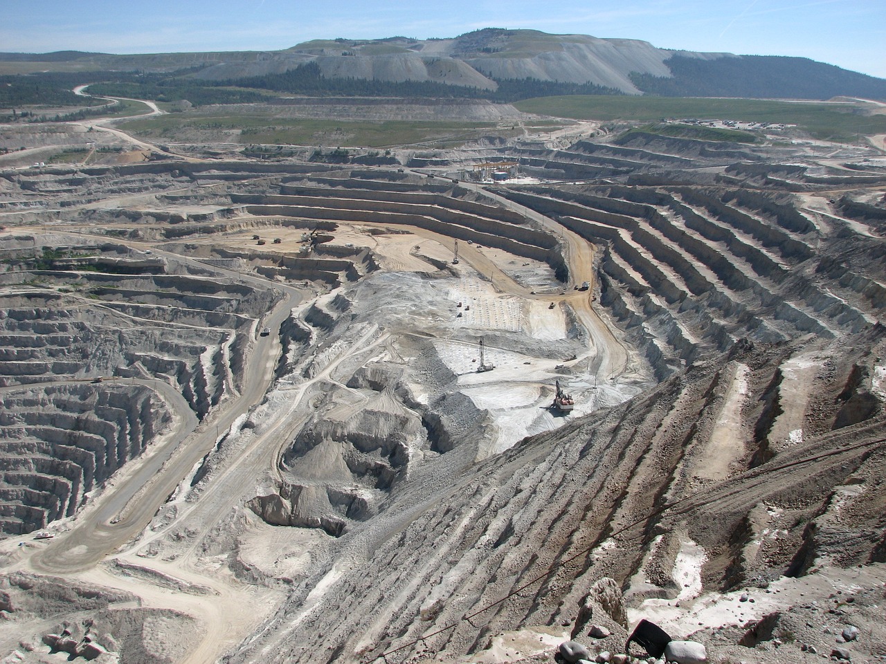 Aerial view of open pit mine during the daytime with an excavator in sight.